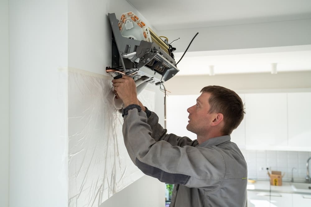 Man technician worker in uniform fixing repairing apartment air conditioner, installing wall-mounted